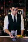 Молодой элегантный бармен, работающий за барной стойкой, смешивая напитки с фруктами — стоковое фото