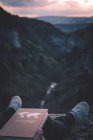 Vue sur la petite rivière dans le canyon et les jambes de la personne avec le livre assis sur le bord — Photo de stock