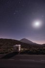 Кемпер припаркований на узбіччі віддаленої пустелі під приголомшливим сяючим місяцем і зоряним небом — стокове фото
