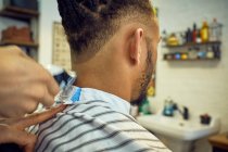 Вид на урожай со спины анонимного парикмахера, делающего современную стрижку бритвой безликому африканско-американскому клиенту — стоковое фото