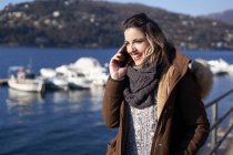 Young woman in winter clothes talking on the phone outdoors next to a lake in Milan Italy — Stock Photo