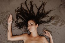 Femme nue couchée sur sable mouillé sur le bord de la mer — Photo de stock