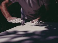 Руки анонимного художника-мужчины, распространяющего грубую белую штукатурку на ровную поверхность в мастерской — стоковое фото