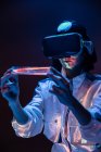 Aufgeregte junge Frau mit Prisma und Virtual-Reality-Erfahrung im Neonlicht — Stockfoto