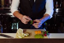 Crop anonyme jeune barman élégant travaillant derrière un comptoir de bar préparer des fruits pour les boissons cocktail — Photo de stock