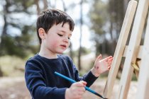 Мальчик рисует на мольберте в деревне — стоковое фото