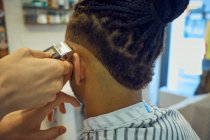 Vista da colheita por trás do cabeleireiro Anônimo fazendo um corte de cabelo moderno com uma navalha para um cliente afro-americano sem rosto — Fotografia de Stock