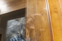 Schöne und junge Frau reflektiert in einem Fenster ihres Hauses und lächelt — Stockfoto