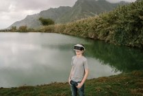 Young adolescent playing a virtual reality simulation with vr glasses standing near a lake — Stock Photo