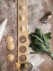 Bunch of ripe sorrel and various utensils placed over flour near uncooked raviolis and dough on kitchen table — Stock Photo