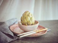 Knife and fork with whole fresh artichoke on pink ceramic plate — Stock Photo