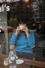 Снаружи фото стильной женщины, пьющей кофе, в кофейне, смотрящей в сторону — стоковое фото