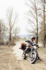 Masculino no capacete equitação rápido moto no empoeirado campo estrada perto de folhosas árvores no natureza — Fotografia de Stock
