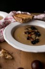 Тарелка восхитительного каштанового супа с грибами и салфеткой на деревянной столешнице . — стоковое фото