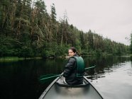 Junge lächelnde Frau blickt beim Bootfahren auf Waldfluss in Finnland zurück — Stockfoto