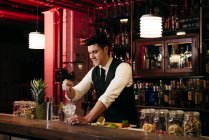 Jovem barman elegante trabalhando atrás de um balcão de bar misturando bebidas com frutas — Fotografia de Stock