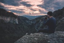 Homem com câmera de foto sentado na montanha colina com pôr do sol magnífico — Fotografia de Stock