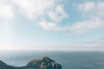 Живописный вид на скалу с естественными арками и дом на вершине, окруженный морем, днем в пасмурный день — стоковое фото