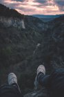 View to small river in canyon and legs of person sitting on the edge — Stock Photo