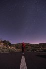 Traveler in red hooded jacket standing on empty road at night — Stock Photo