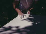 Mãos de artista masculino anônimo espalhando gesso branco áspero na superfície lisa na oficina — Fotografia de Stock