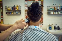 Вид з поля позаду анонімного перукаря, який робить сучасну стрижку з бритвою для безликого афроамериканського клієнта — стокове фото
