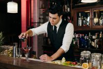 Молодий елегантний бармен, що працює за барною стійкою, наливає напій від шейкера до келиха — стокове фото