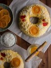 Bowls with fresh egg yolk and sugar crystals placed on lumber table near delicious uncooked Rosca de Reyes with candied fruits. — Stock Photo