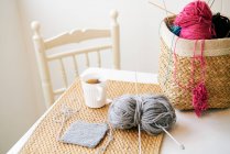 Cup of warm tea placed on table near basket with knitting yarn and needles in cozy room — Stock Photo