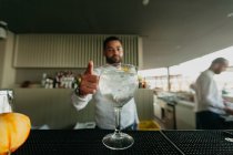 Fröhlicher Mann bereitet in einer Bar mit erhobenem Daumen ein alkoholisches Getränk zu — Stockfoto