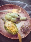 Closeup of halved fresh artichoke and sprouts on pink ceramic plate on table — Stock Photo