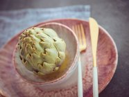 Closeup of knife and fork with whole fresh artichoke on pink ceramic plate — Stock Photo