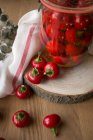 Still life with jar of tasty pickled pimientos peppers placed on piece of wood near fabric napkin and plant sprig. — Stock Photo