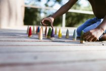 Unrecognizable shirtless African American boy sitting on wooden surface and playing with colorful cones on sunny day — Stock Photo