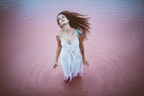Jovem mulher bonita com cabelos longos encaracolados usando vestido de verão apreciando brisa do mar — Fotografia de Stock