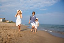 Щасливі і усміхнені діти в повсякденному вбранні бігають босоніж уздовж берега моря на піщаному пляжі в літній сонячний день — стокове фото