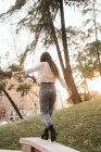 Молода жінка в повсякденному вбранні розтягує руки, балансуючи на паркані в сонячний день в парку — стокове фото