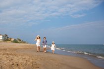 Bambini felici e sorridenti in abbigliamento casual che corrono a piedi nudi lungo la spiaggia sabbiosa in estate giornata di sole — Foto stock