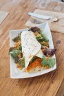 Апетитний варений вегетаріанський рулет зі здоровою свіжою морквою та салатом на білій тарілці на дерев'яному столі в кафе — стокове фото