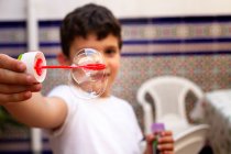 Little boy in white T-shirt playing soap bubbles while standing on terrace at home — Stock Photo
