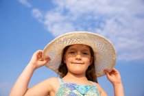 Von unten niedliches Mädchen in blauem Strickkleid und breitkrempigem Hut, das im Sommertag steht — Stockfoto