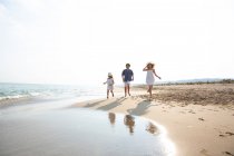 Happy and smiling children in casual wear running barefoot along seashore on sandy beach in summer sunny day — Stock Photo