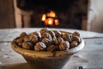 Bowl of natural organic nuts on wooden table near fireplace in ancient village house — Stock Photo
