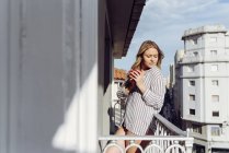Молода весела жінка з чашкою на терасі — стокове фото