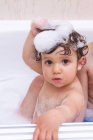 Entzückendes Baby blickt mit nassen Haaren in die Kamera, während es im Badezimmer badet — Stockfoto
