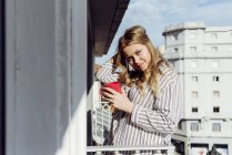 Молодая веселая женщина с чашкой на террасе — стоковое фото