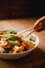 Bol de plat végétarien savoureux avec des légumes avec baguettes main femelle — Photo de stock