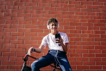 Joven hombre negro feliz escuchando música con smartphone en bicicleta - foto de stock