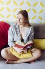 Молода щаслива жінка читає книгу на дивані — стокове фото
