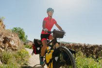Lady in sportswear and helmet riding bike on stony path while traveling through forest on sunny day in countryside — Stock Photo